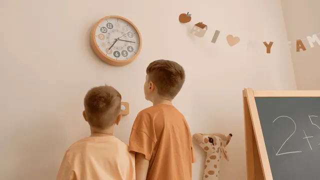 Routime-Kinderwanduhr an einer Wand, mit zwei Kindern davor